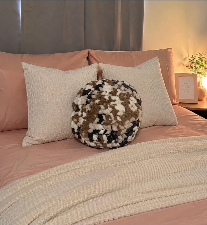 Round camouflage hand-knit statement pillow on a bed