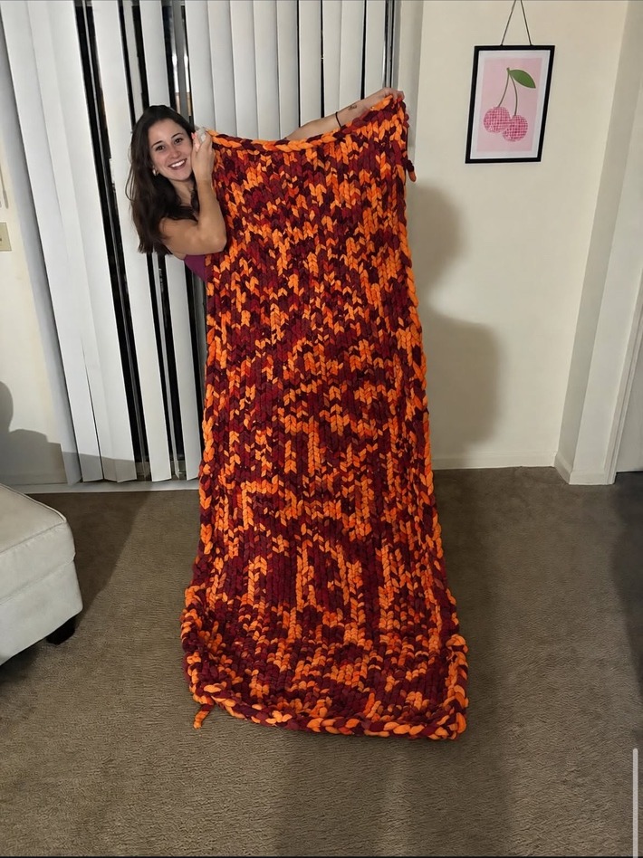 Sarah holding a large maroon and orange hand-knit Hokie blanket